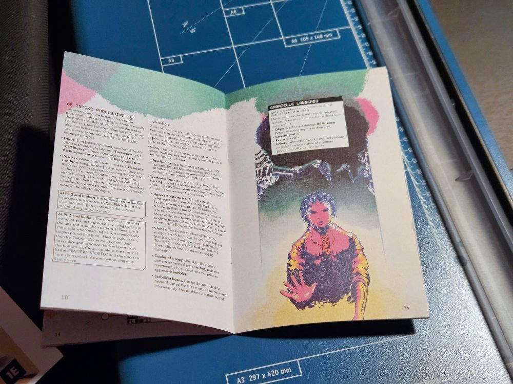 A neat home-made booklet of Emergence placed on a paper cutting machine. The booklet is opened and shows a spread of pages, showing off both text and illustration.