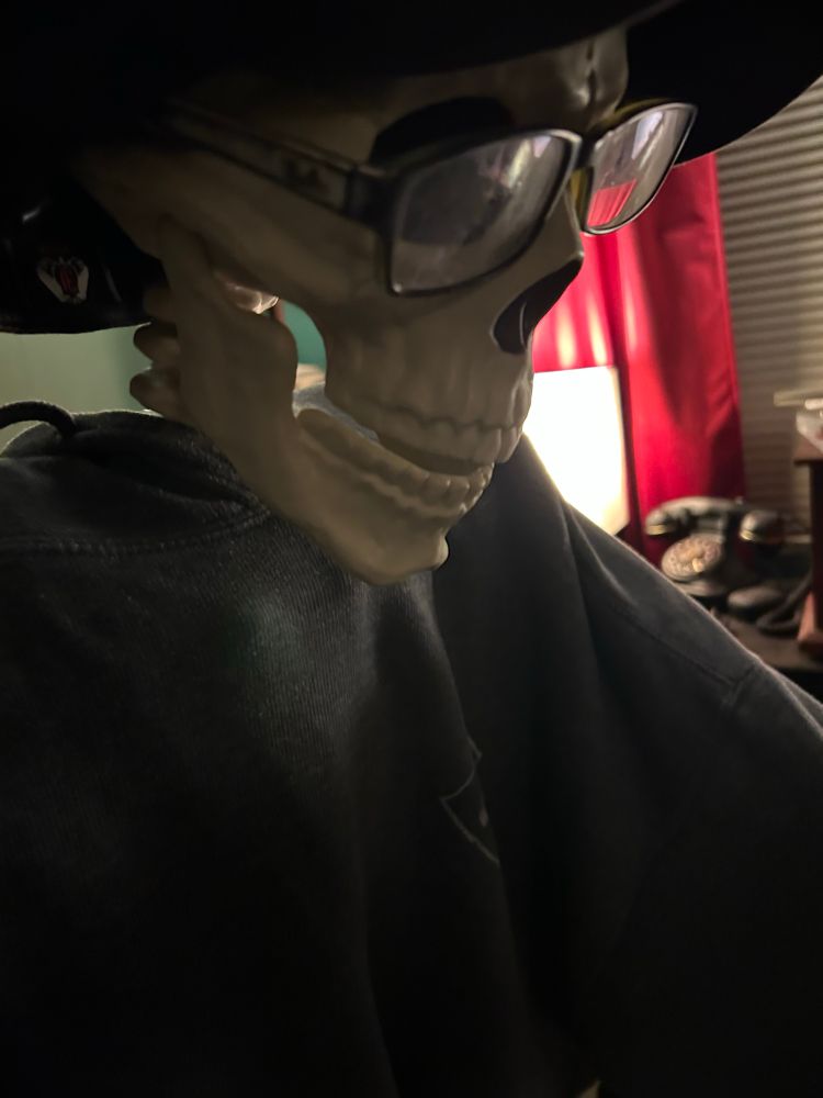 A close up of the “face” on a fake, plastic skeleton dressed in a hoodie, glasses and a hat.