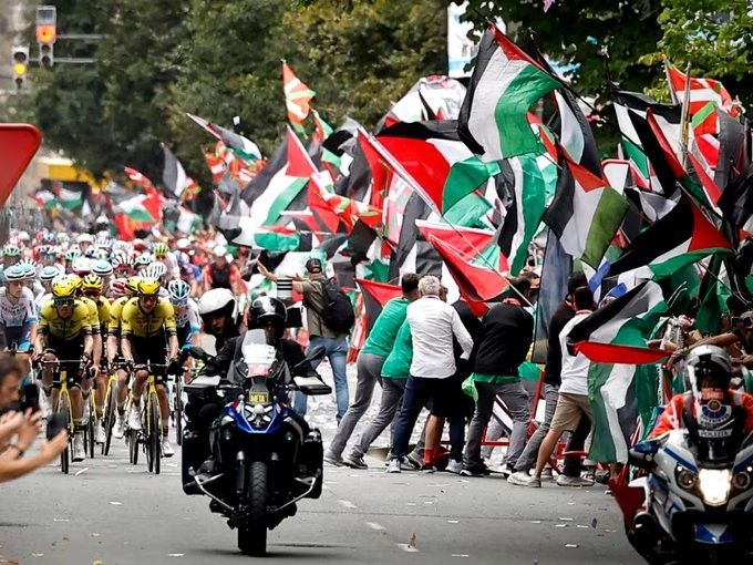 Banderas palestinas se desbordan hacia la calzada con los ciclistas de la Vuelta mientras ertzainas de paisanos los intentan contener