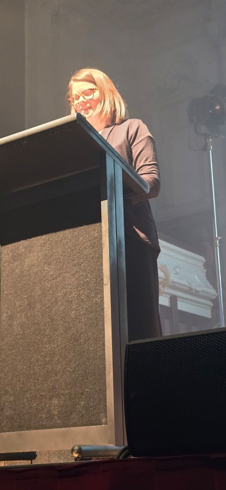 Jada Watson behind lectern and reading. 