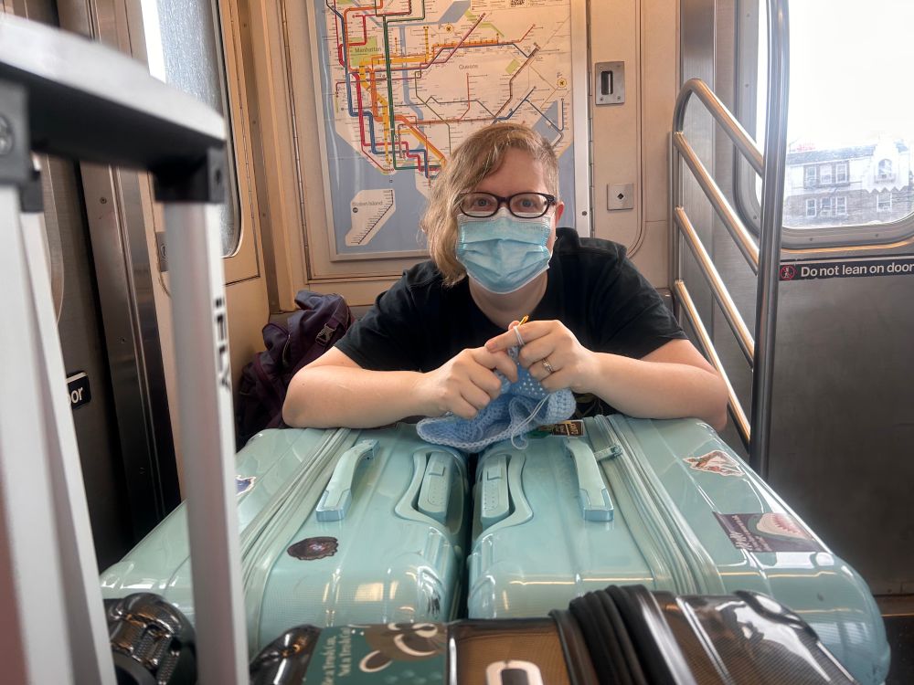 Ashlie, crocheting over top two giant suitcases with the subway map behind her on the wall.