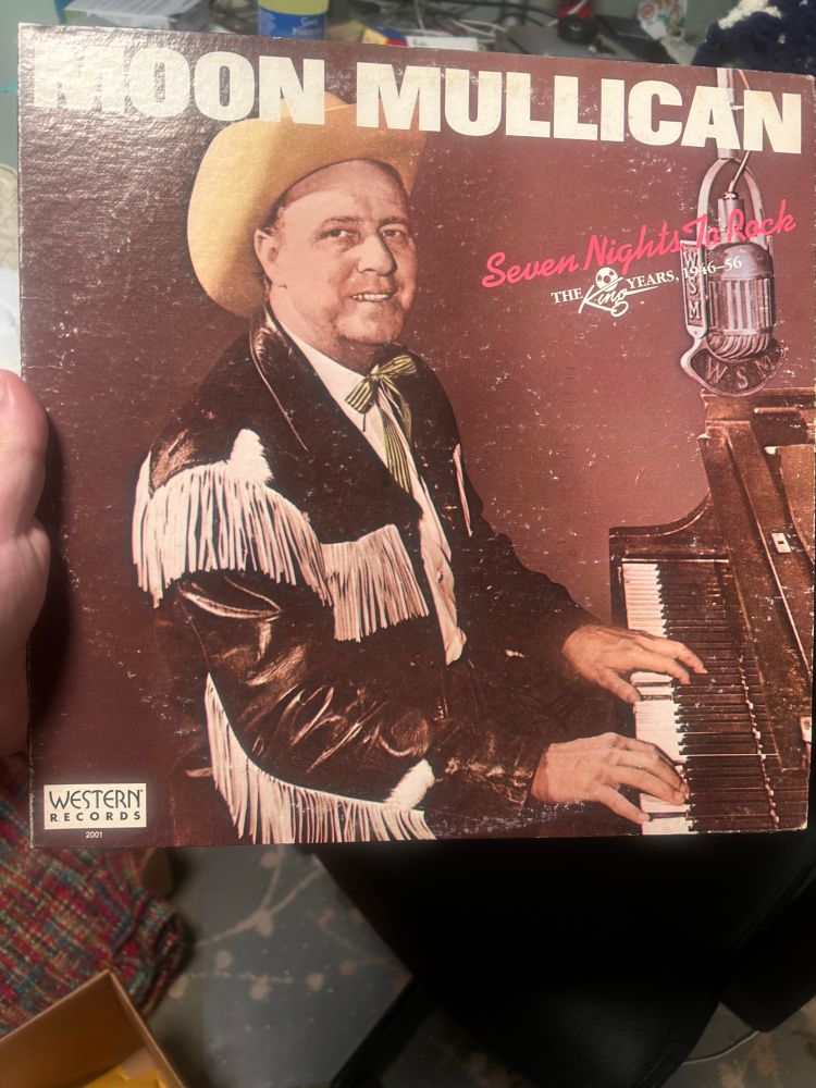 Moon Mullican’s Seven Nights to Rock album featuring a middle aged man in a western fringe shirt and cowboy hat sitting at a piano