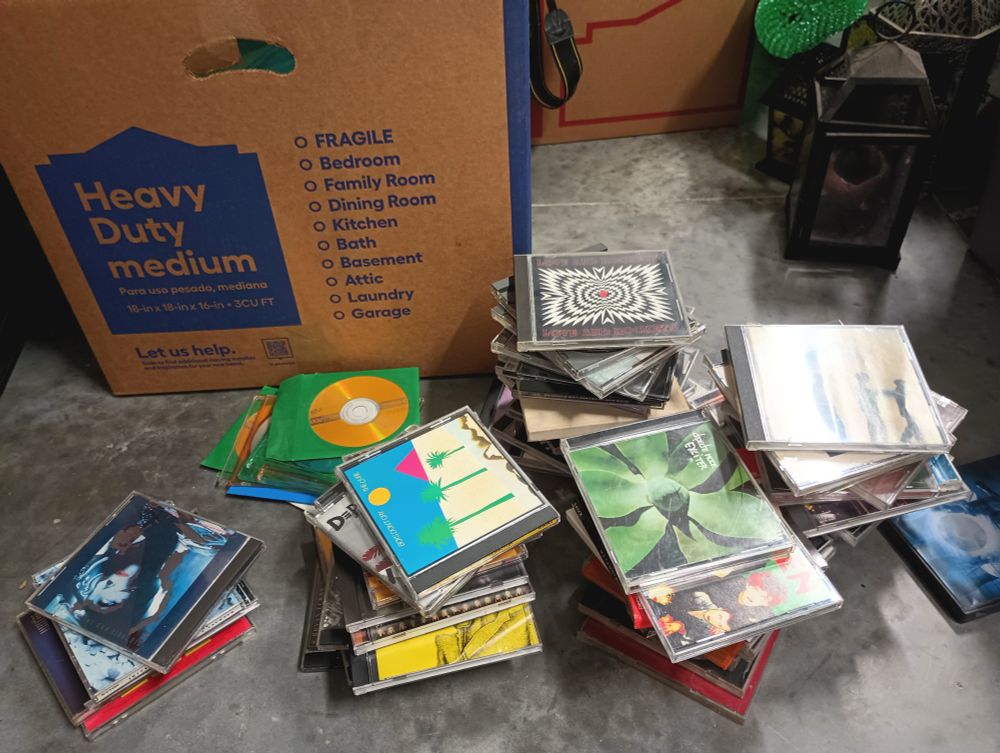 Six piles of CDs sit loosely stacked on the garage floor. Visible are copies of albums by Siouxsie and the Banshees, the Cure, Depeche Mode, Love and Rockets and Echo and the Bunnymen. The last pile is all burned CDs most of which have no label.