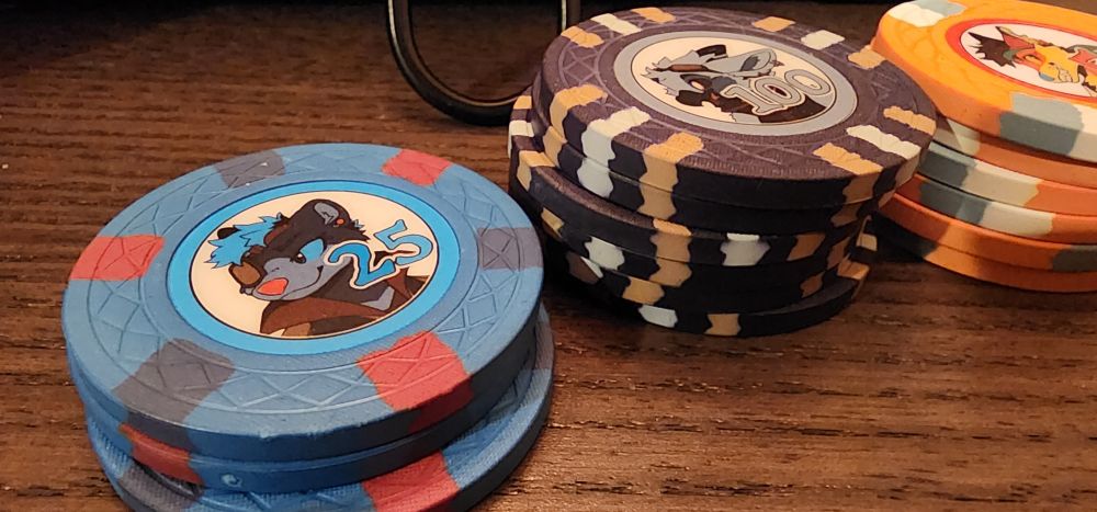 Close-up of the blue 25 point chip and black 100 point chip. The blue 25 chip features an image of AWU mascot Carver. The black 100 chip features AWU mascot Spike. Both characters are in pirate garb.