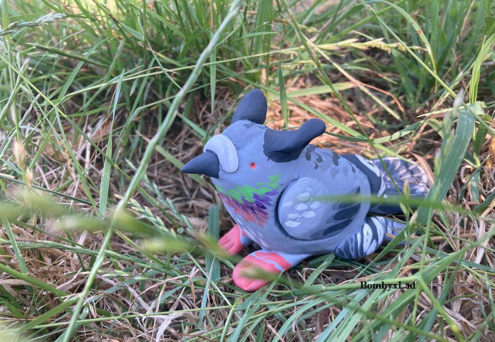 [ID: this sculpture is a pigeon gryphon; like a grey pigeon with paws for the hind feet, cat ears, and bird tail. end ID]
