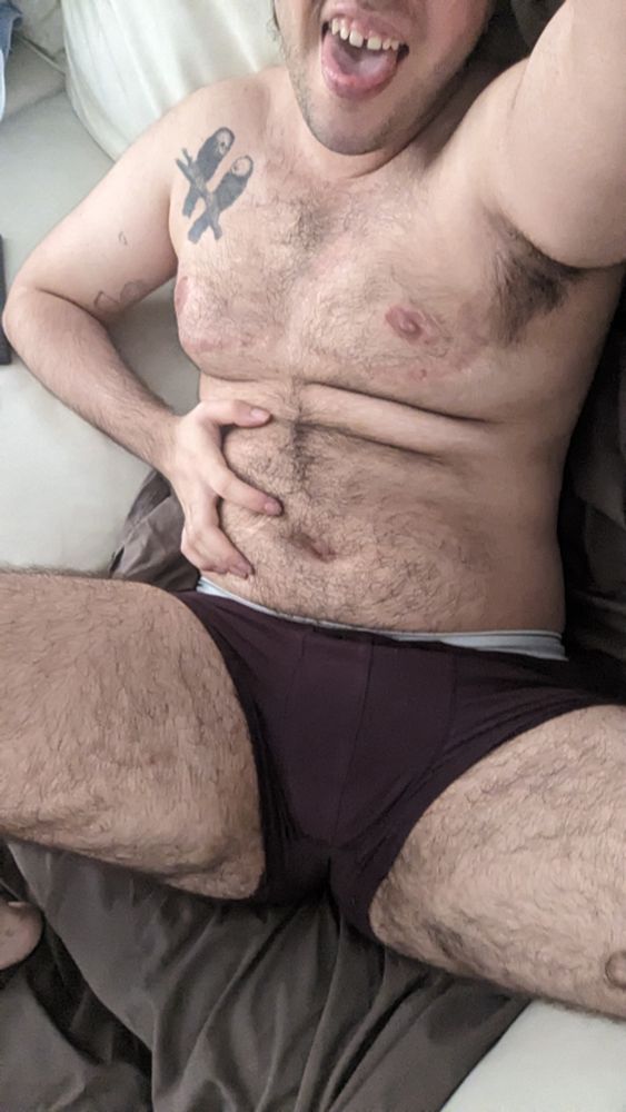 A selfie of me laying on a sofa wearing only dark red boxers. with the hand on my left I'm grabbing my tummy 