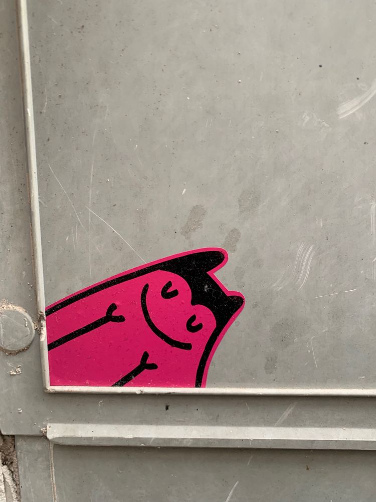 Graue Wand, darauf eine Art Street-Art Hase als schwarze Strichzeichnung, rosa angemalt, lächelt zufrieden. 