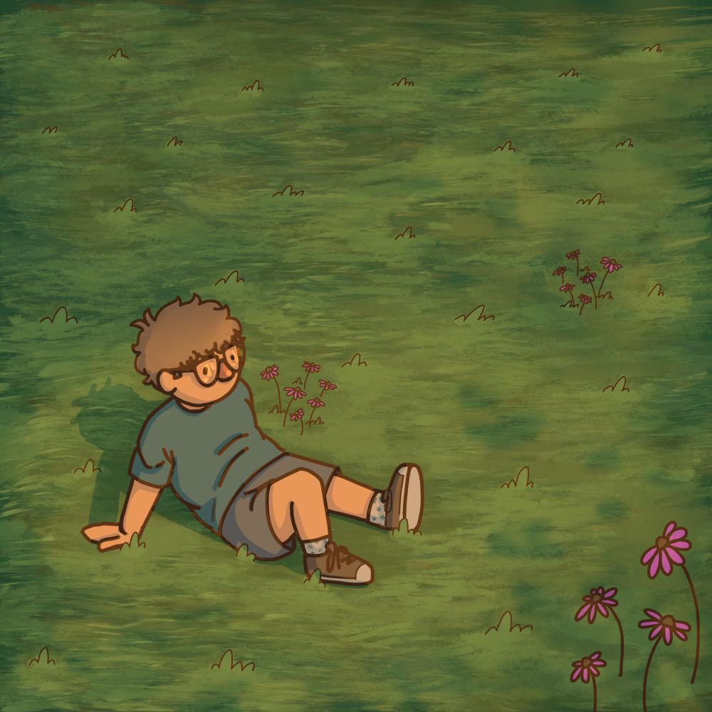 Blond man wearing a blue shirt and gray shorts lays in a field with a few pink flowers. 