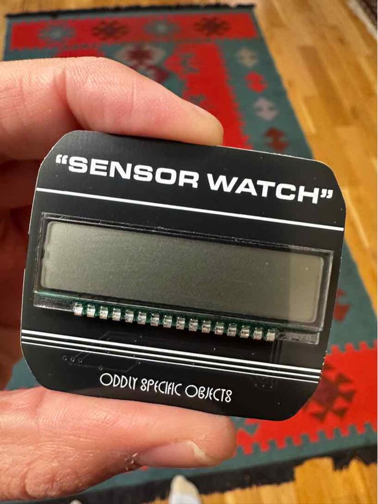 Photo of a small gadget with a screen. Text on the gadget reads “Sensor Watch” in quotes. 