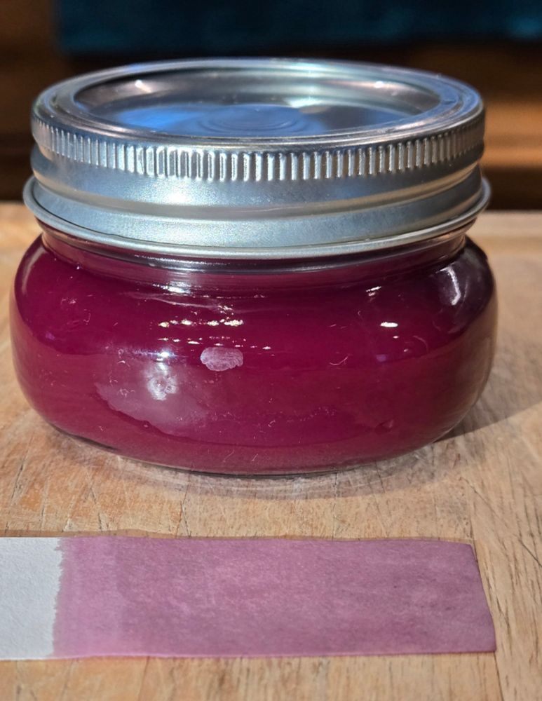 A jar of purple ink made from rose petals and a test strip showing the lavender color it makes on paper. 