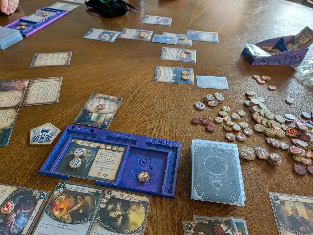 A bunch of cards laid out on a table. Many locations are represented, with a few trays and tokens representing different game pieces. 