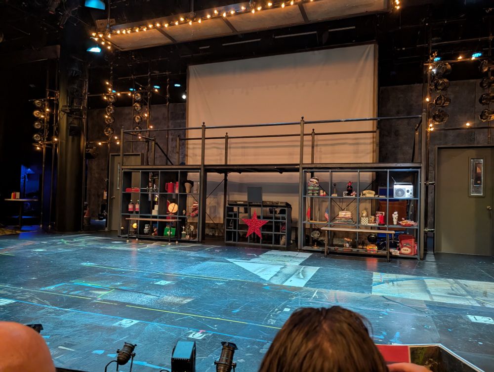 A stage with a bunch of lights, a set of shelves with various ephemera on them, and a red star in the middle next to a keyboard. 