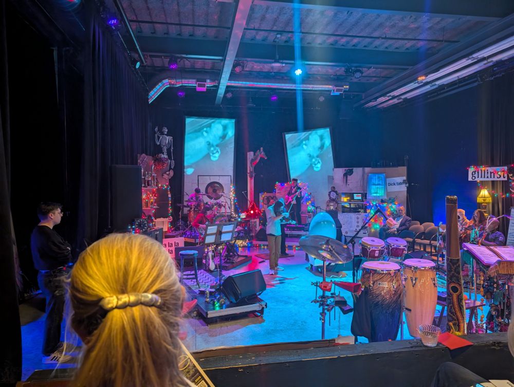 A stage setup with multiple instruments, a wide open space and a lot of eccentric ephemera. 