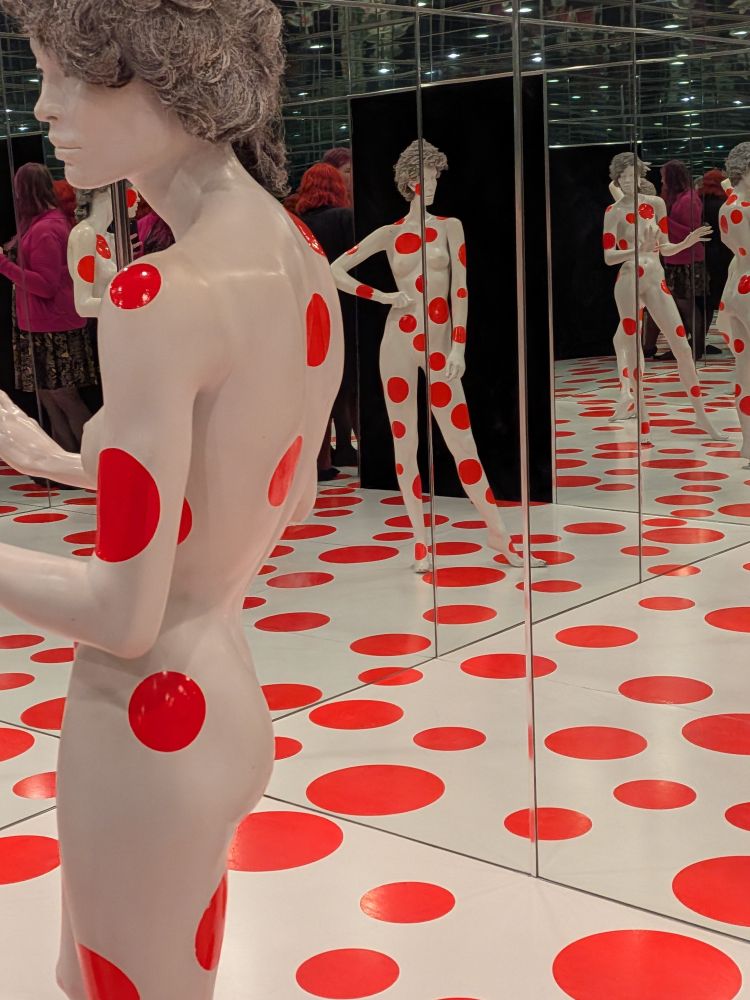 An "infinite" room by Yayoi Kusama with some white mannequins and many red polka dots on the floor and mannequins. 