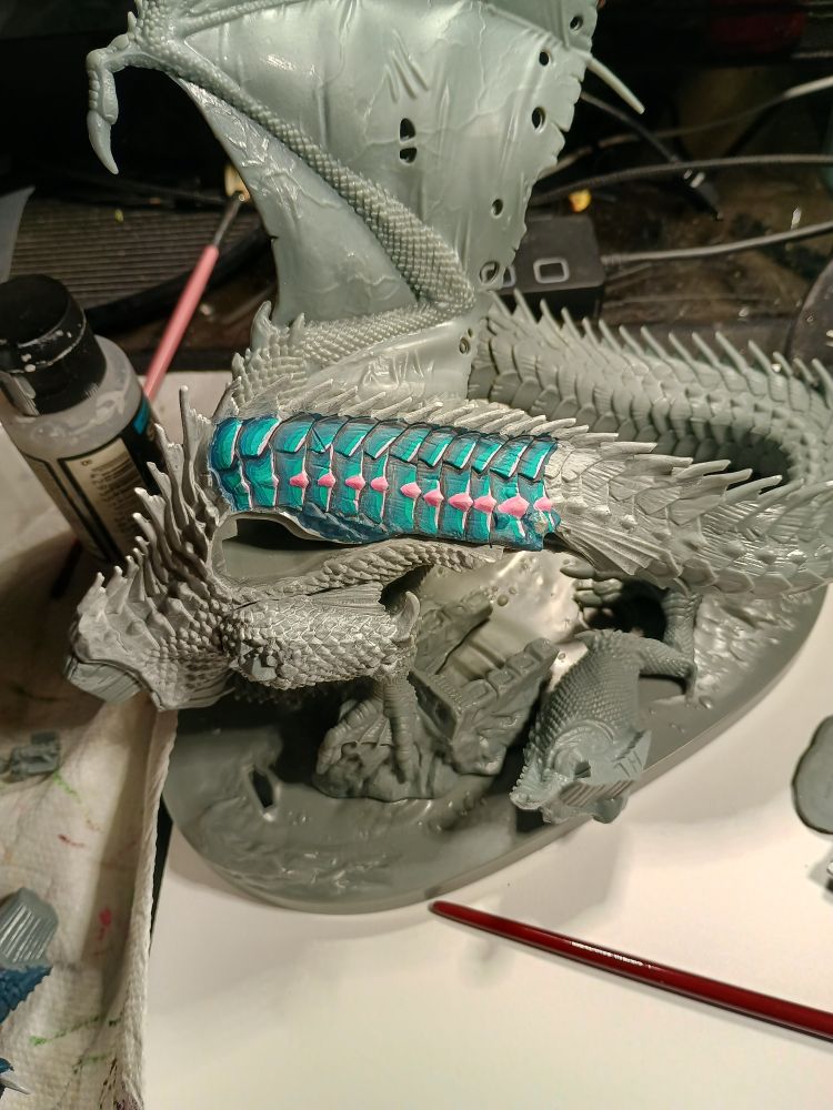 partially assembled, partially painted, extra large dragon miniature. the painted section is teal with pink nubs
