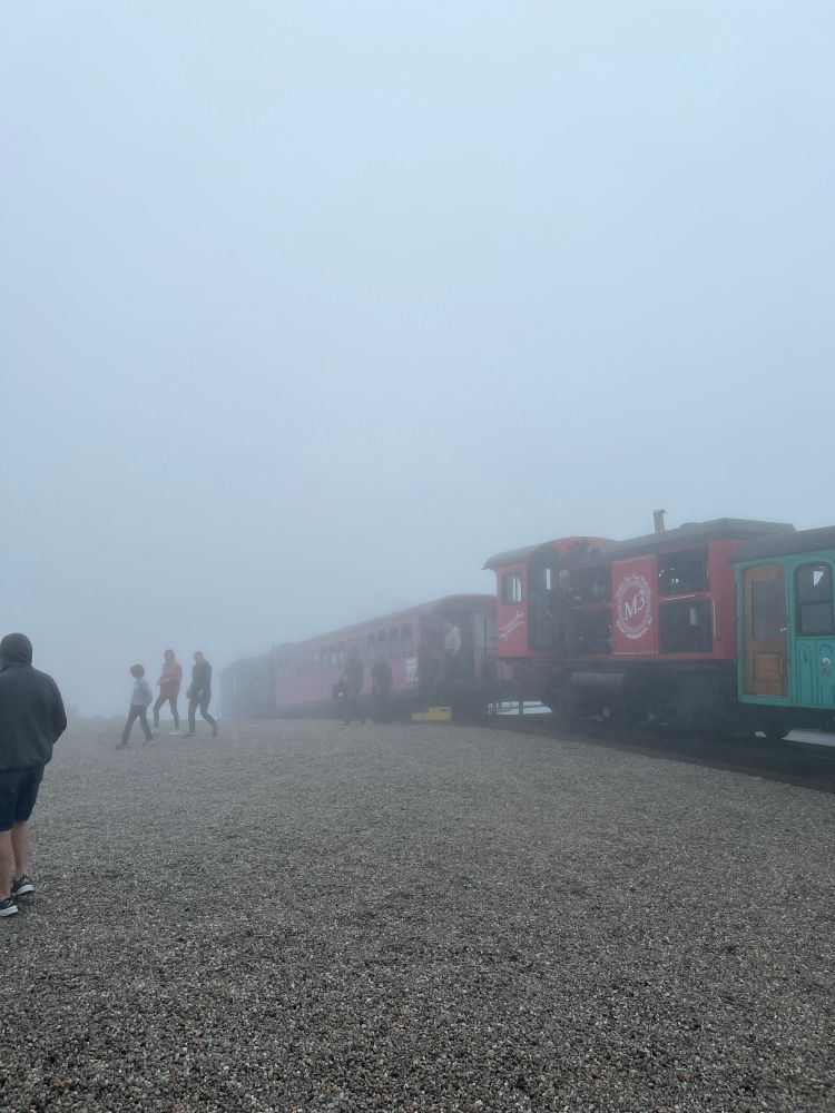 Summit of Mount Washington covered in clouds. Two train cars are stopped on the tracks
