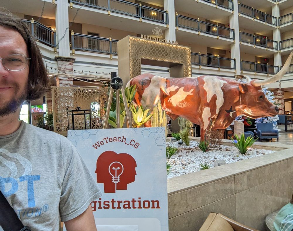 A selfie next to the WeTeachCS conference registration with a cow in the background 