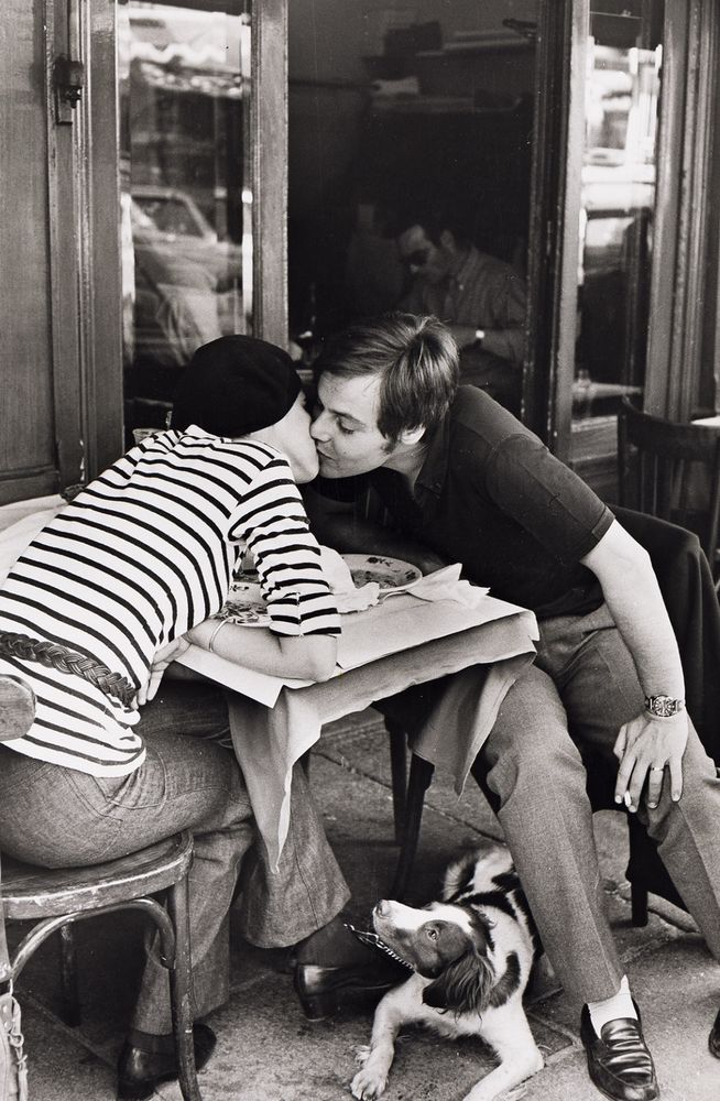 A couple kissing in a Paris street outdoor café, a dog looking on