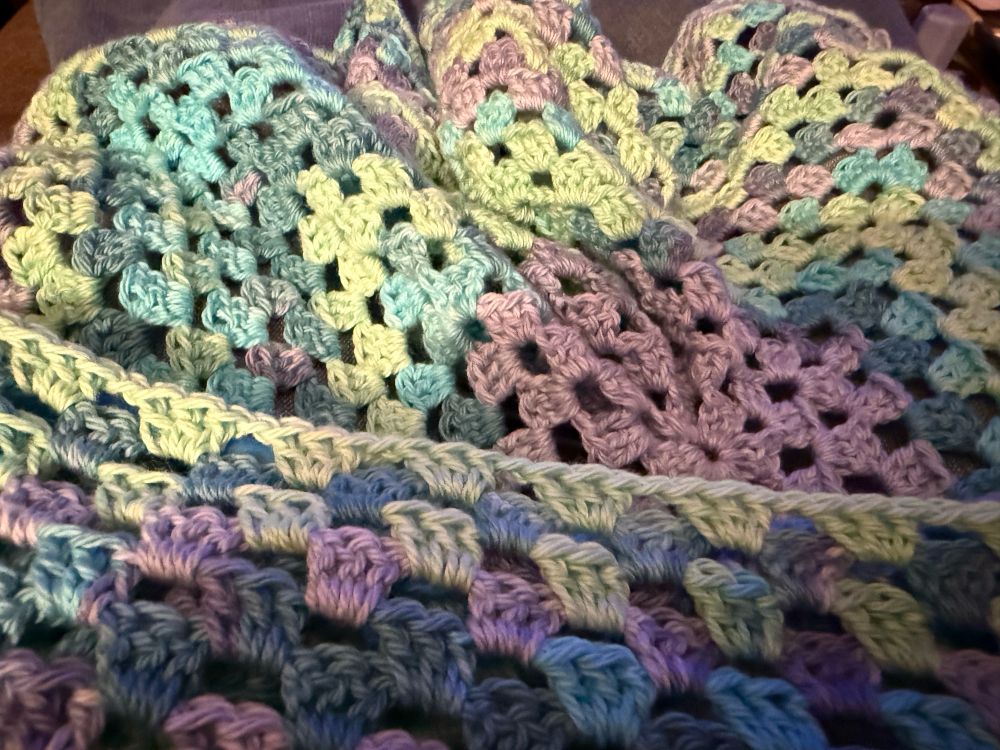 crochet in granny square style in a mix of blue, purple, and light green. 