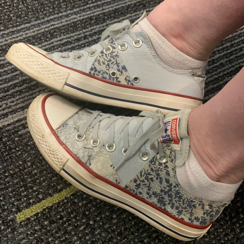 My feet on a striped commercial carpet in low top Chuck Taylor sneakers. They are light blue patchwork with a couple different floral fabrics and light blue laces 