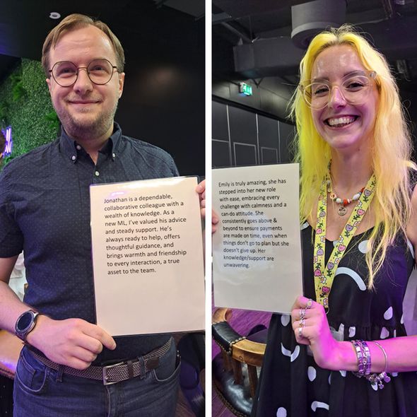 A man with glasses and a beard smiles at the camera while holding a white sign that describes him as "Jonathan," a dependable, collaborative colleague with warmth and friendship. To his right, a woman with bright yellow hair and glasses smiles broadly, holding a sign describing "Emily" as amazing, calm, and having unwavering knowledge and support.