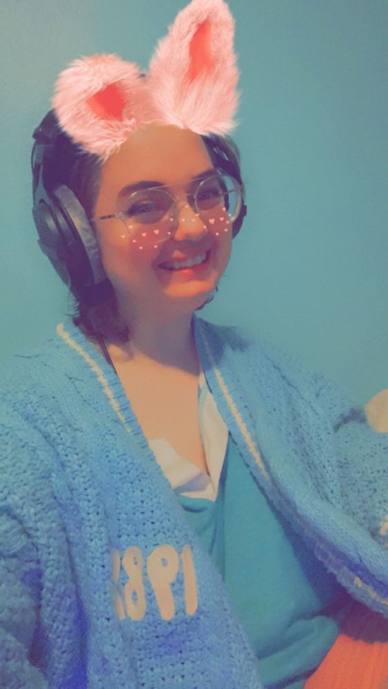 a brunette girl with a bunny filter and headphones wearing the 1989 swiftie cardigan 
 
