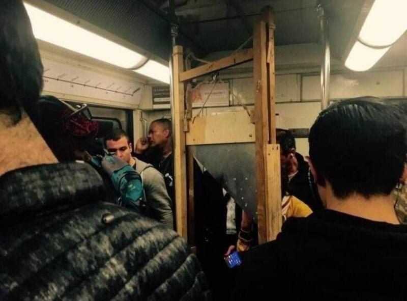 Passengers in a rail compartment stand around a full gullotine.
(It was on the Metro in Paris, to explain why no one looks bothered.)