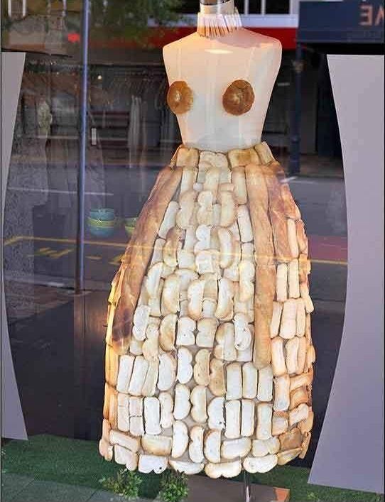 A tailor's dummy in a dress shop window. The top is bare save for two doughnuts at chest level, but there's a full-length skirt that looks like it's made entirely of different types of bread slices and full French loaves