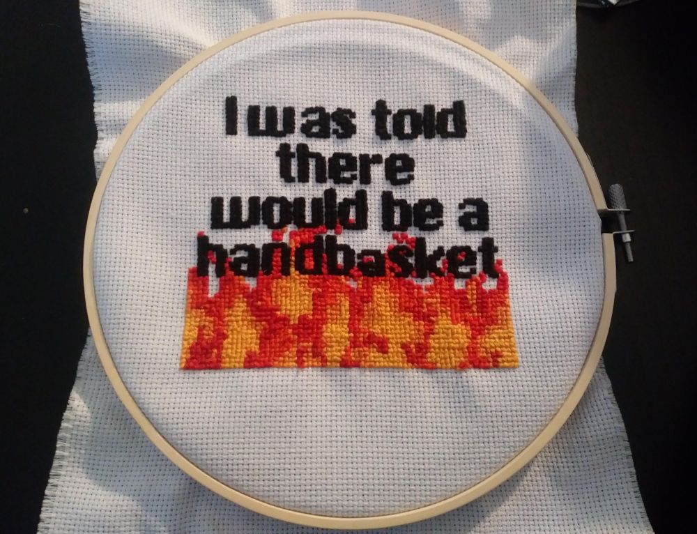 Embroidery ring with
"I was told
there
would be a
handbasket"
in cross-stitch, with the final word above red and yellow "flames"