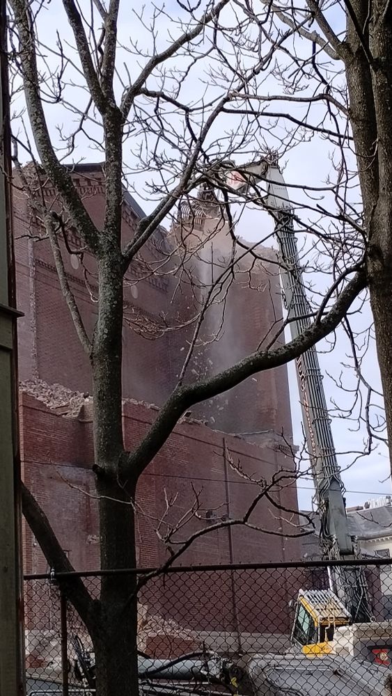 A cloud of debris as a crane takes out a chunk of the rear of the church 