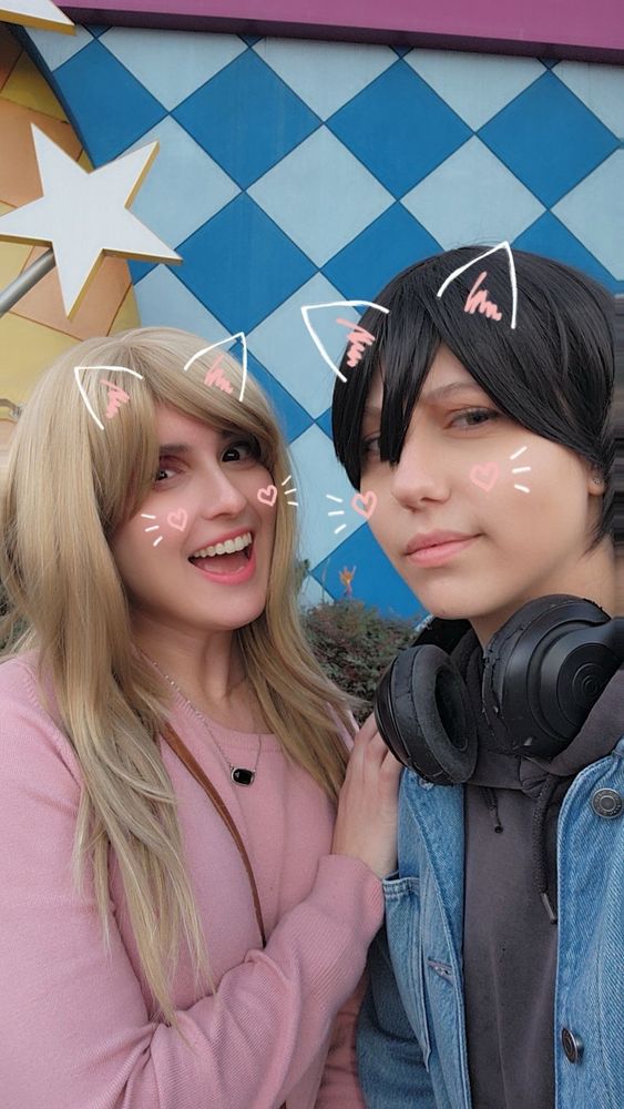 Person with blond hair and a pink sweater standing next to a person with short black hair and a black hoodie
