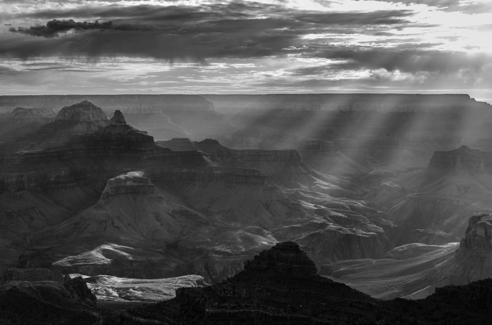 Black and white photo of the sunrise in the Grand Canyon with scenic crepuscular rays shining through the clouds