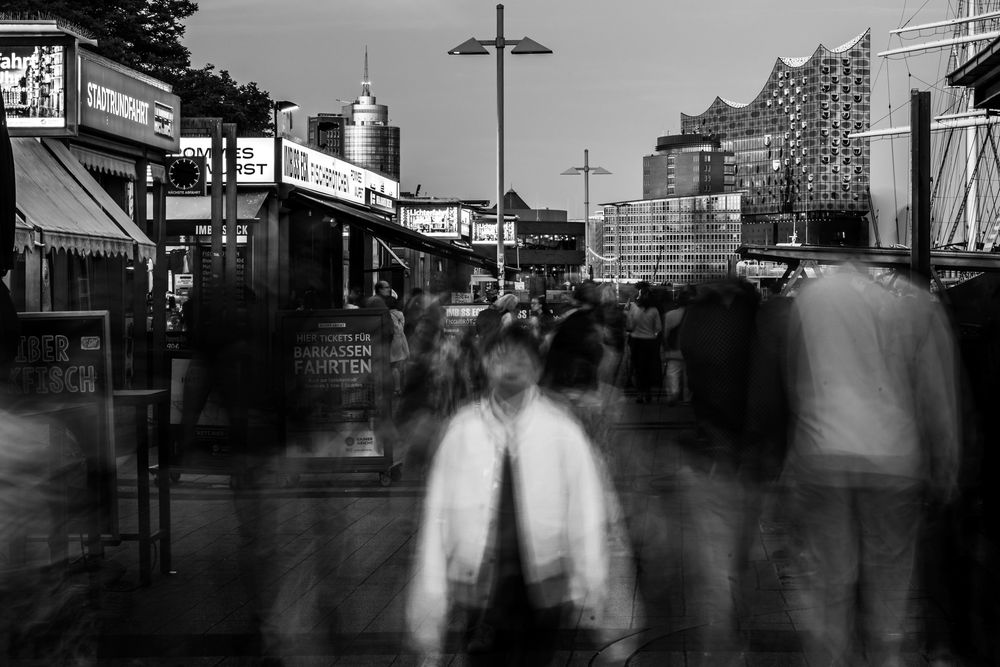 Black and white long exposure photo of people walking along the waterfront at St. Pauli Landungsbrücken in Hamburg