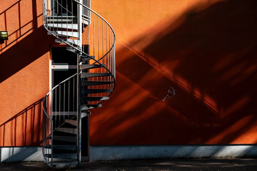 Photo of an orange house wall with a metal spiral staircase in the foreground