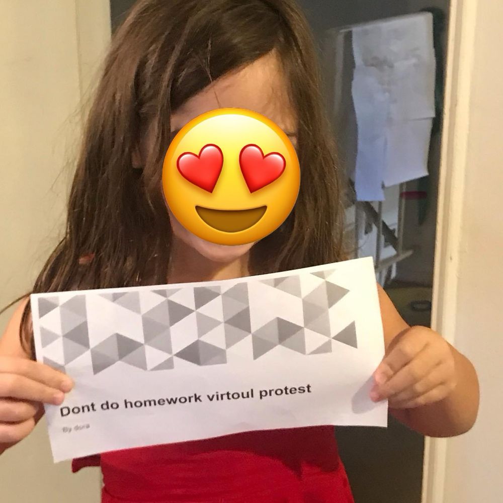 Small girl holds sign reading “Don’t do homework virtuoul protest.” Her face is obscured by an emoji with heart eyes.