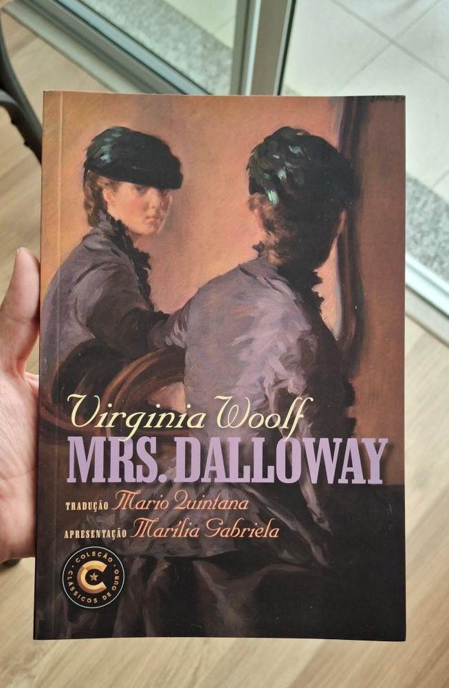 "mrs dalloway" da virginia woolf. a capa é uma mulher com vestido roxo e chapéu preto com penas verde escuro se olhando no espelho. conseguimos ver ela de costas, mas seu rosto aparece no reflexo do espelho.