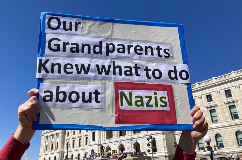 Hands holding sign in front of St. Paul Capitol that says "Our Grandparents Knew What To Do about Nazis"