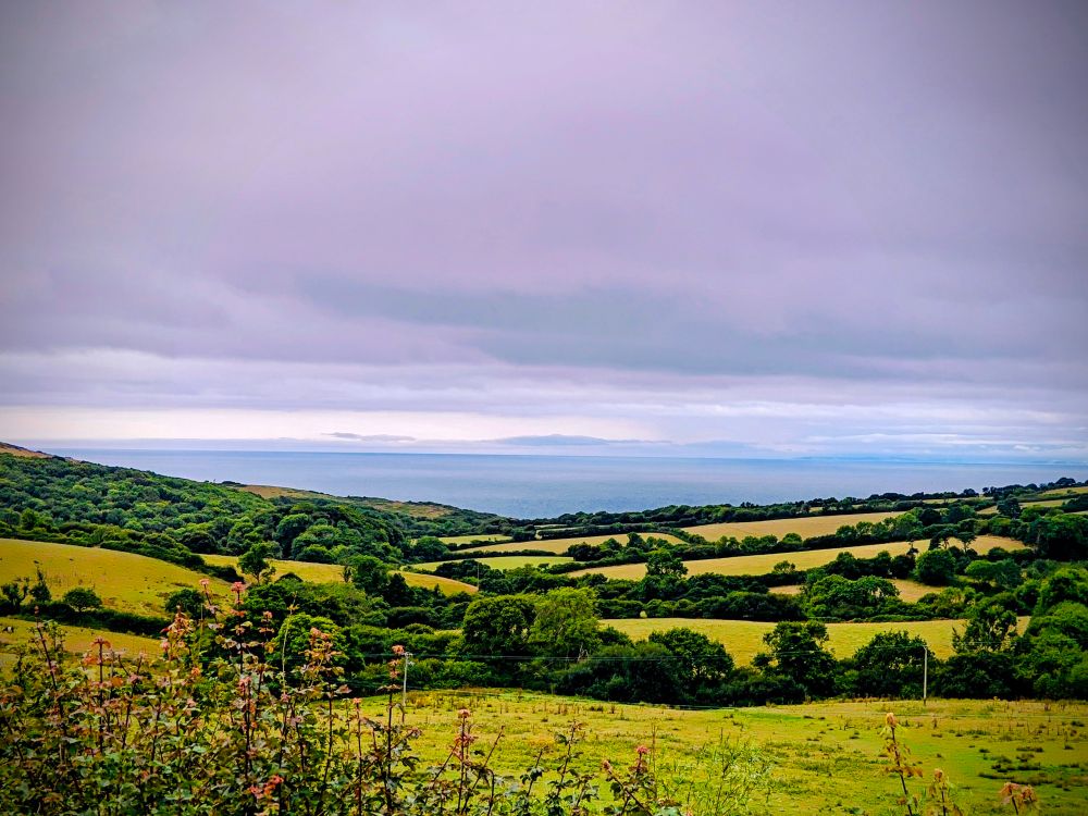 A view of rolling farming countryside with the grey sea in the distance. 