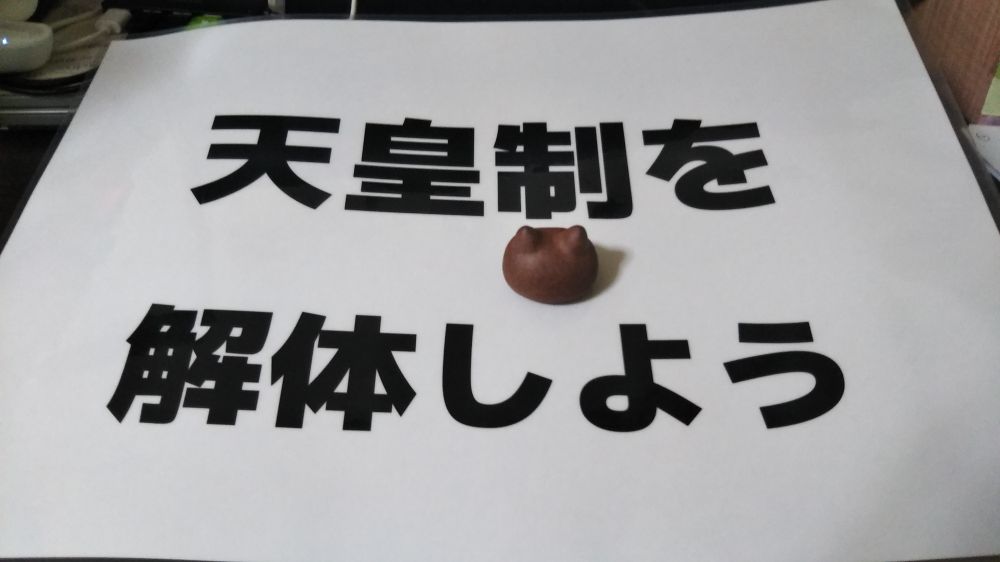 「天皇制を解体しよう」と書かれたプラカードにねこの置物（じよもにゃん）が添えられた写真