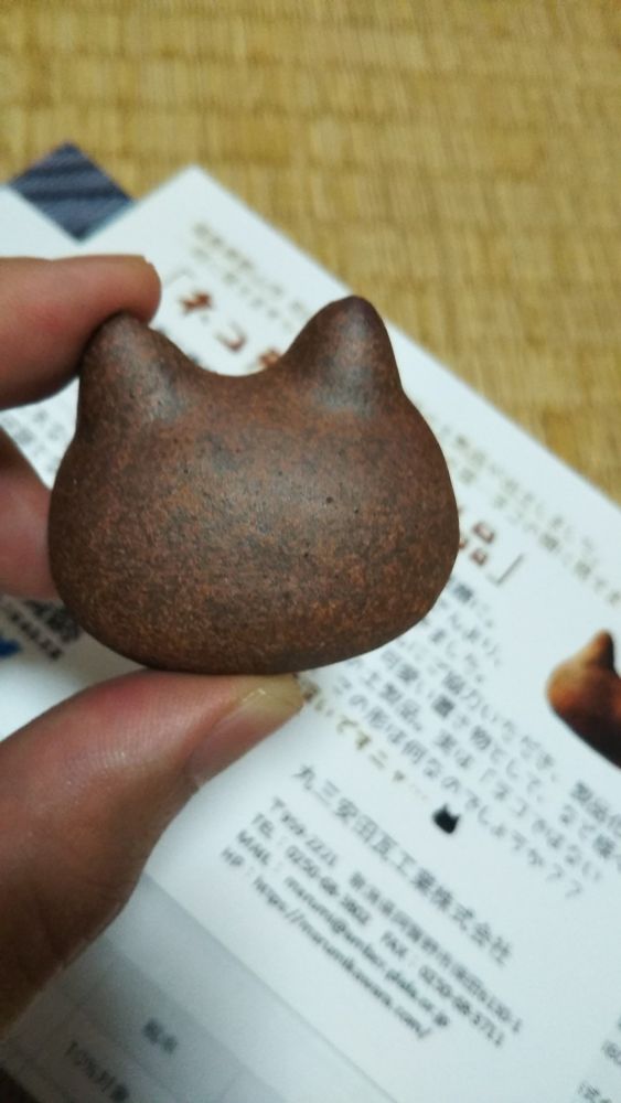 ねこ型らしき土製品の置物を左手の人差し指と親指でつまんでいる写真。