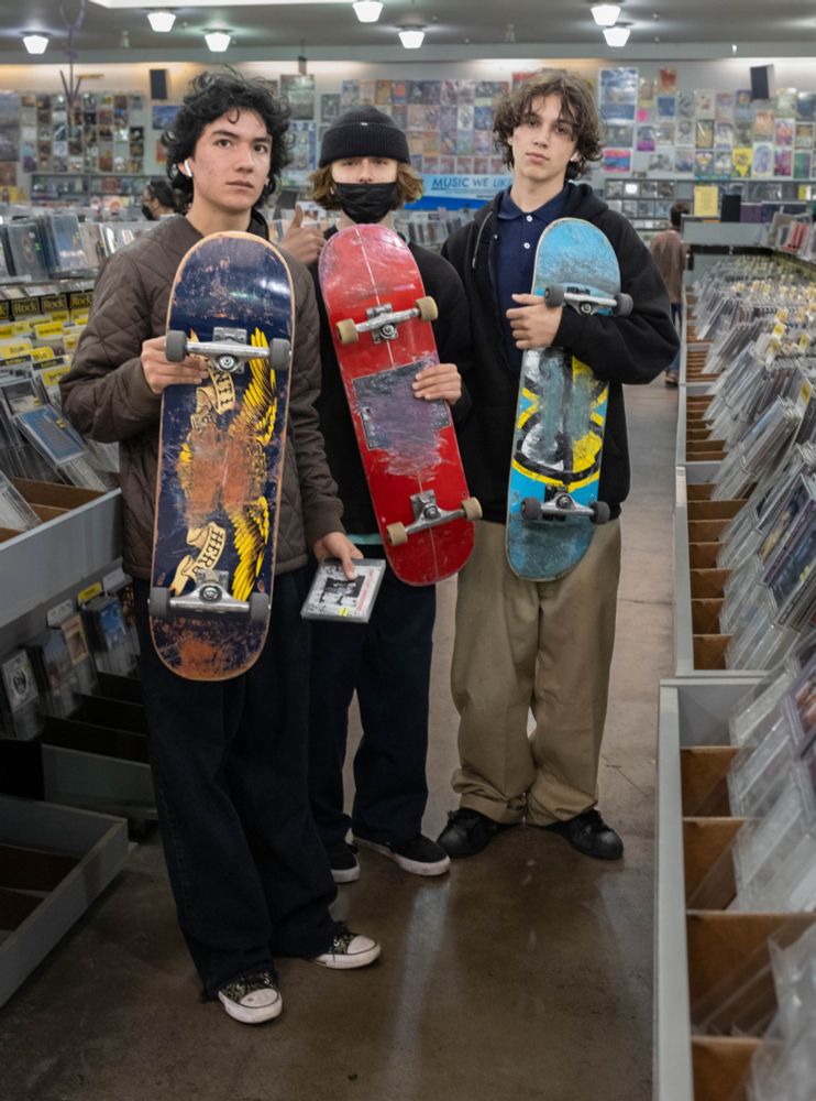 Three teenage skateboarders holding their boards, standing in Amoeba Records Store in San Francisco's Haight Ashbury.