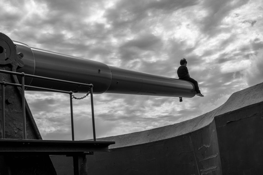 Little boy sitting on edge of cannon looking out at storm clouds at Fort Casey, Whidbey Island, Washington State