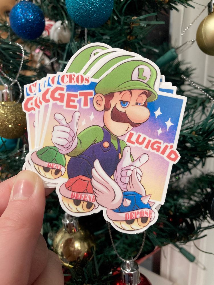 photo of Nicole Brennan (Artist) holding a sticker of Luigi from Super Mario Bros. He has his hands on finger guns, and there’s a green, red, and blue shell in front of him that say “deny, defend, depose”. Text on the sticker says “CEOs get Luigi’d”.