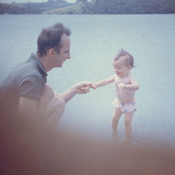 Man holding the hand of a toddler at the beach.
