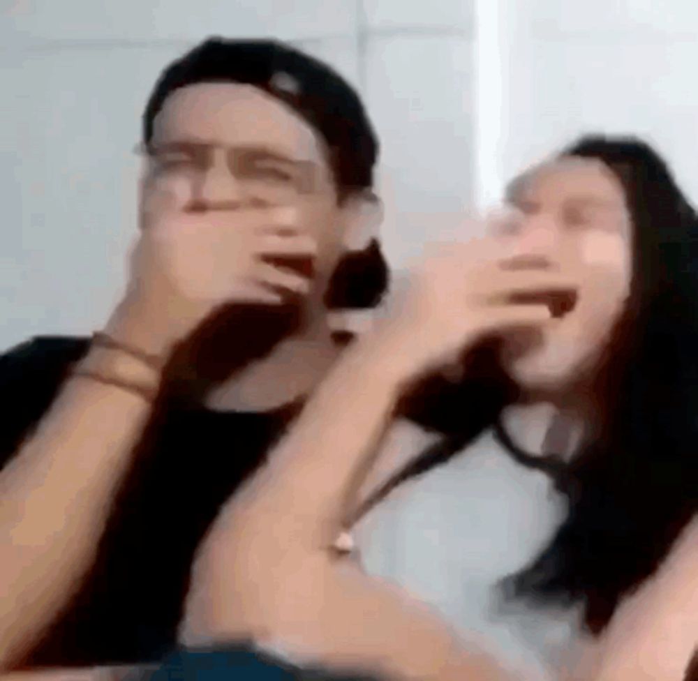 a man and a woman are laughing together and covering their mouths with their hands .