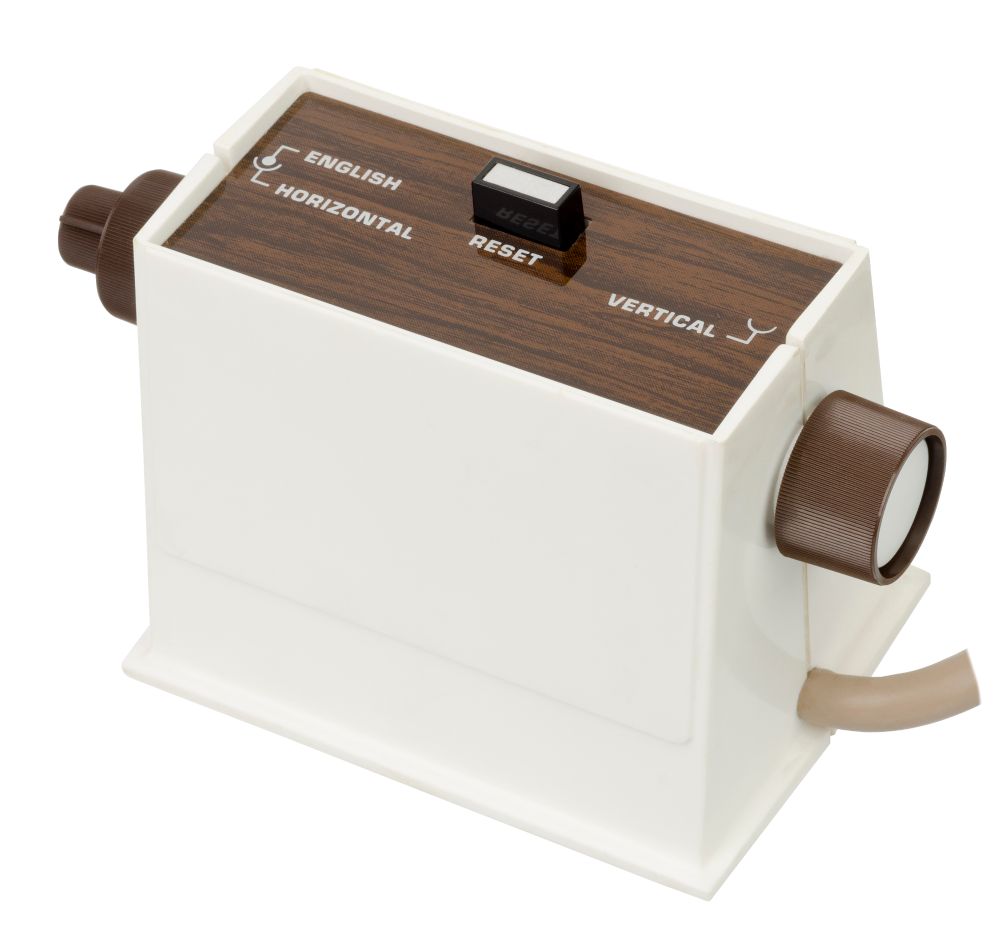 The Magnivox Odyssey controller: a tall, white trapezoidal solid with a thick wire coming out of it at the bottom right, a dial above that marked vertical, a dial on the left labeled horizontal with a smaller dial inside it labeled "English" and a center rectangular button labeled reset. All the button functions are printed in capital letters on a wood patterned sticker atop the box.