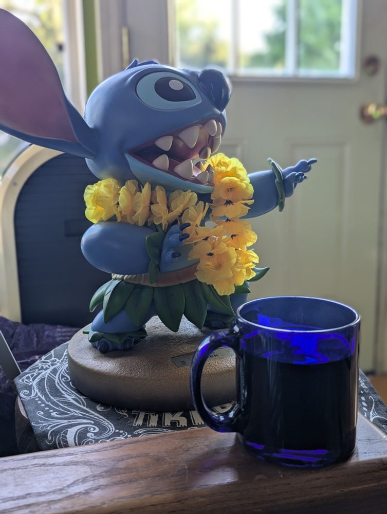 A large maquette of Disney's Stitch with a steaming mug of coffee in the foreground