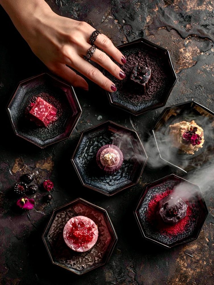 Description and prompt: An overhead shot of a surreal tasting ritual of five otherworldly candies arranged on obsidian plates, two faintly steaming. A single hand reaches into the frame with precision. --chaos 15 --ar 3:4 --raw --stylize 150