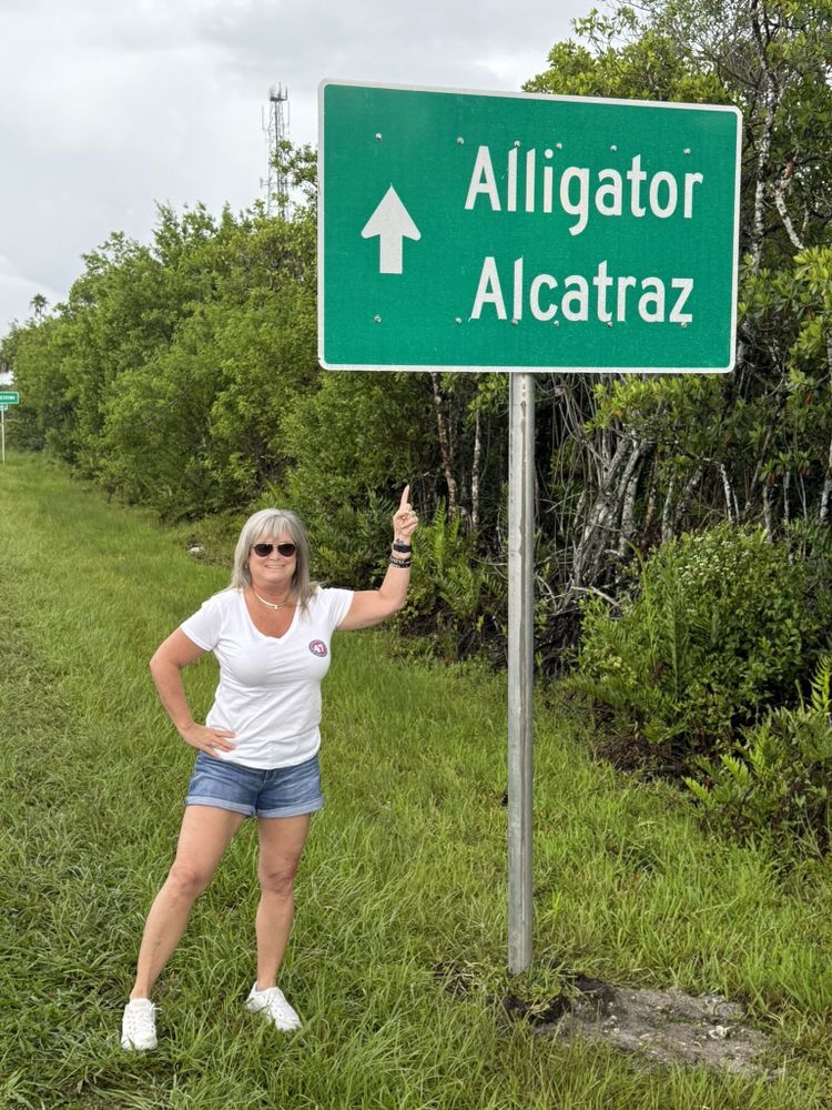 A woman in a Trump shirt standing next to an Alligator Alcatraz sign