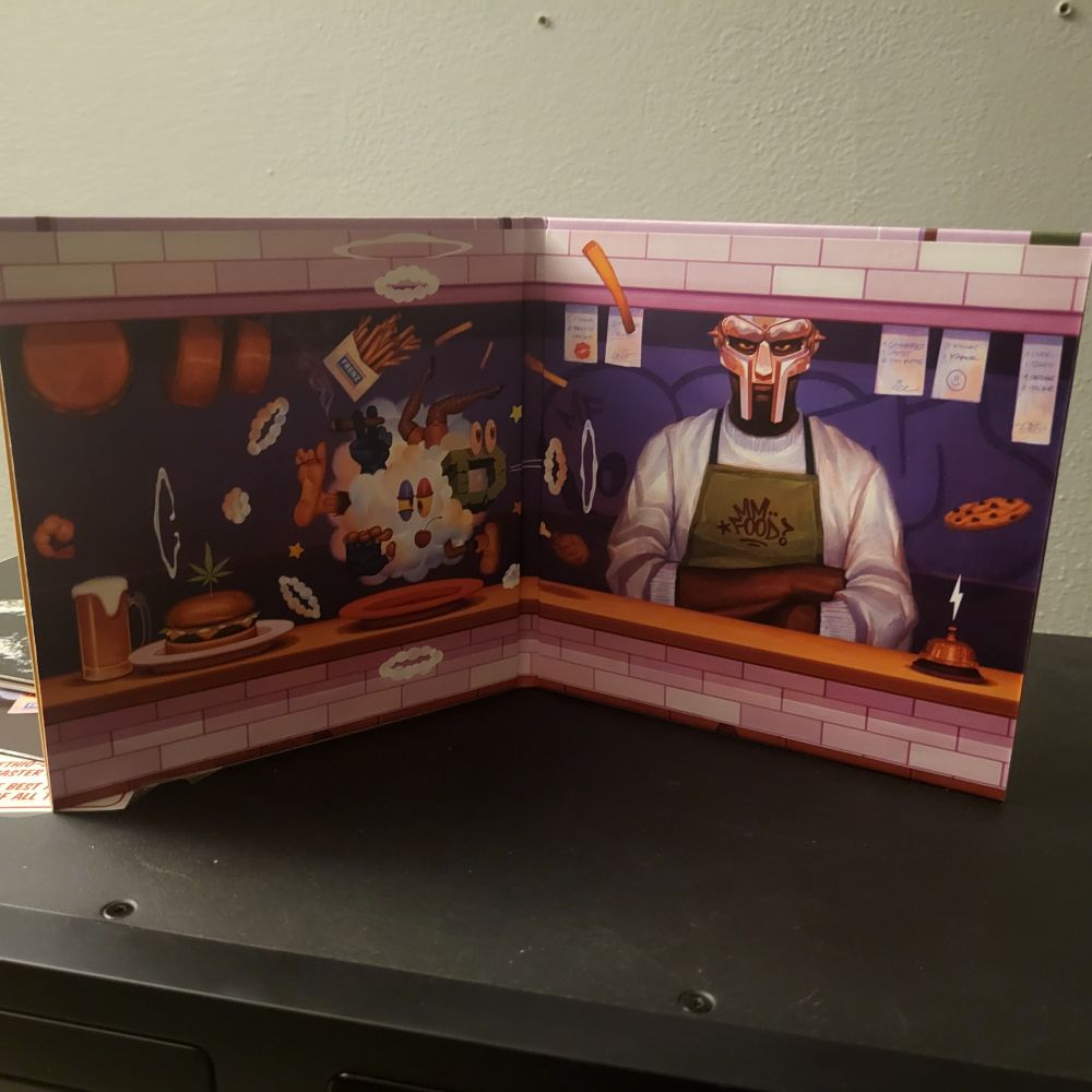 Middle gatefold of the 2024 CD reissue of MF DOOM's MM...FOOD which shows a comic illustration of DOOM behind a diner cook counter